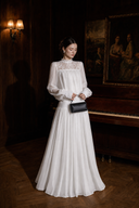 VOGSION Isolde Victorian-inspired white lace maxi dress photographed in a dark piano room.
