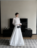 VOGSION Isolde white high-neck lace maxi dress with long semi-sheer sleeves and a flowing lined skirt.