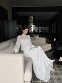 VOGSION Isolde long-sleeve white cotton lace maxi dress styled seated, showing its lined flowing skirt.