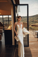 Adult woman wearing an ivory plunge neck maxi dress in a full-length front view by an open doorway