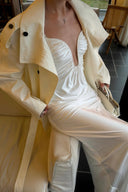 Seated close-up of an ivory ruched maxi dress beneath a light coat