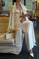 Seated view of an ivory plunge neck maxi dress styled with a light coat