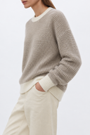 Side view of Liorine oatmeal wool sweater showing dropped shoulders, ivory rib cuffs and natural untucked hem
