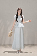Model wearing the VOGSION Mirelle Light Blue puff-sleeve petite peplum maxi dress with a raised waistline.