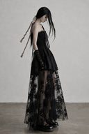 Side view of black corset dress with sheer floral floor-length layer