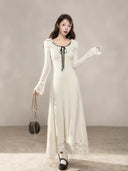 Front view of an ivory petite long sleeve A-line maxi dress with a black neckline bow and lace-trim hem