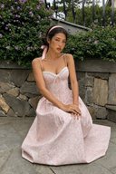     Vogsion Roselle Blush Floral Corset Lace-Trim Midi Dress worn outdoors by a customer in a garden setting with pink floral print and sweetheart neckline