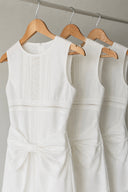 Close-up of the Vogsion Shushu White Linen Statement Bow Petite Midi Dress showcasing premium white linen fabric, intricate pintuck pleats, lace insert, oversized statement bow, and elegant layered skirt. Minimalist petite white midi dress designed for bridal brunches, garden parties, and summer occasions.