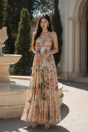 VOGSION Solenne tiered floral maxi dress beside a stone garden fountain