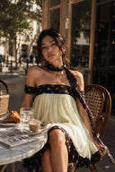 Vogsion Velvandis Off Shoulder Dot Mini Dress (Sage Green Polka Dot) styled at a Paris café, featuring an off-shoulder neckline, flowing babydoll silhouette, lightweight sage green fabric with contrast polka dot trim and scarf detail. Perfect European vacation outfit, summer holiday dress, romantic brunch look and chic resort wear.
