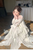 White formal maxi dress with long sleeves and layered petal-inspired ruffles shown while seated