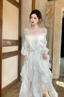 Standing view of VOGSION white layered maxi dress with long sleeves, crystal neckline and silver chain belt