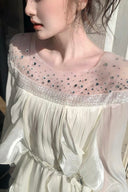 Close-up of the crystal embellished illusion neckline and flowing white fabric on the VOGSION maxi dress