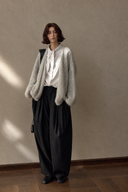 Black pleated wide barrel-leg trousers styled with a white blouse and light cardigan.