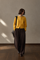 Brown pleated barrel-leg trousers with a yellow cardigan, walking view.