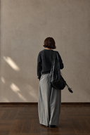 Back view of grey wool-blend barrel-leg trousers styled with a black top and shoulder bag.