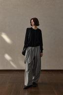 Grey wool-blend barrel-leg trousers styled with a black cardigan, walking view.