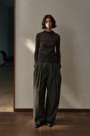 Olive pleated barrel-leg trousers styled with a fitted dark top, front view.