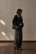 Olive barrel-leg trousers styled with a dark jacket and shoulder bag, side view.