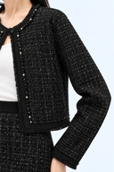Close-up of black tweed texture, round neckline, beaded front trim and fringed jacket edges.