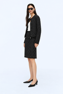 Full-length side view of the black tweed jacket and knee-length skirt set styled with black pointed shoes.