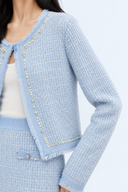 Close-up of light blue and ivory tweed texture, pearl-effect trim and fringed jacket edges.